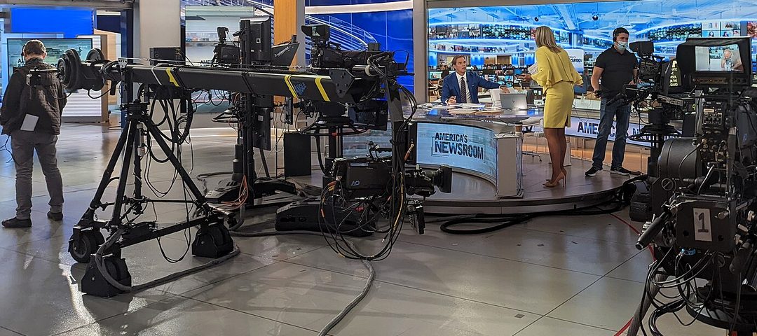 A television newsroom studio floor with cameras and anchors on set.
