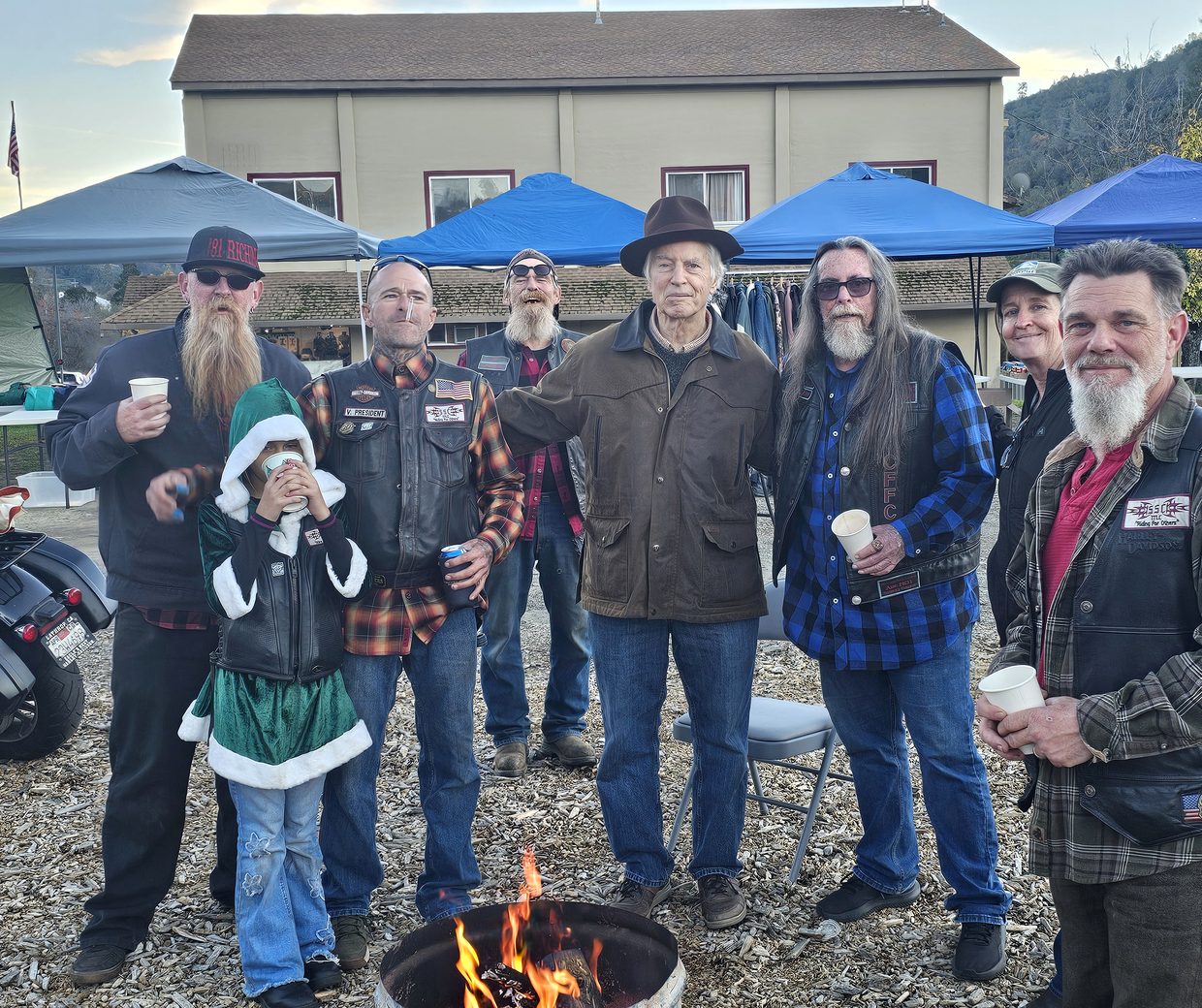 Neighbors gathered around a fire pit at the Frost Shop Marketplace in downtown Mariposa, with the historic building and market tents behind them.